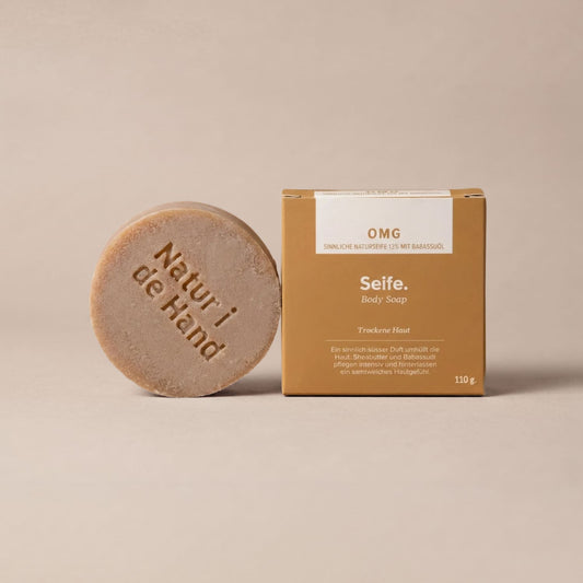 Naturseife OMG von Natur i de Hand – runde sandfarbene Seife mit Prägung «Natur i de Hand» neben ockerfarbener Schachtel
