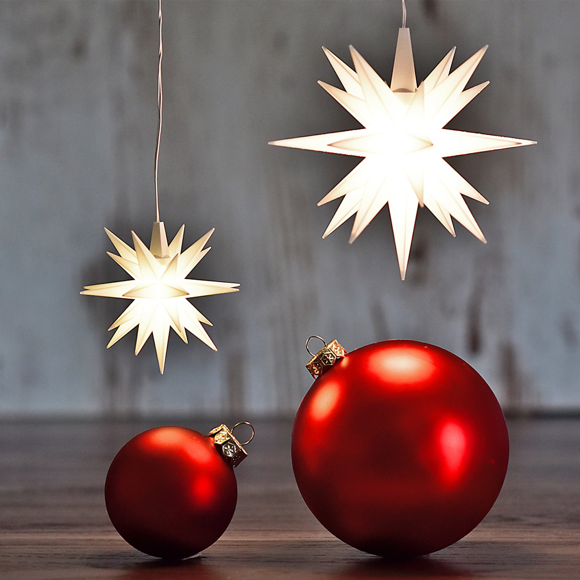 Zwei leuchtende weisse Herrnhuter Sterne über roten Christbaumkugeln