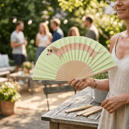 Bei einem Gartenfest hält eine Frau den Dackel-Fächer hoch, im Hintergrund Gäste unter Lichterketten