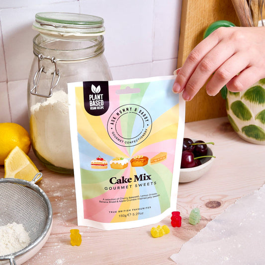 NaniManu Cake Mix Gummis – eine Hand hält den Beutel in einer Backstube neben Mehlglas, Zitronen und Kirschen