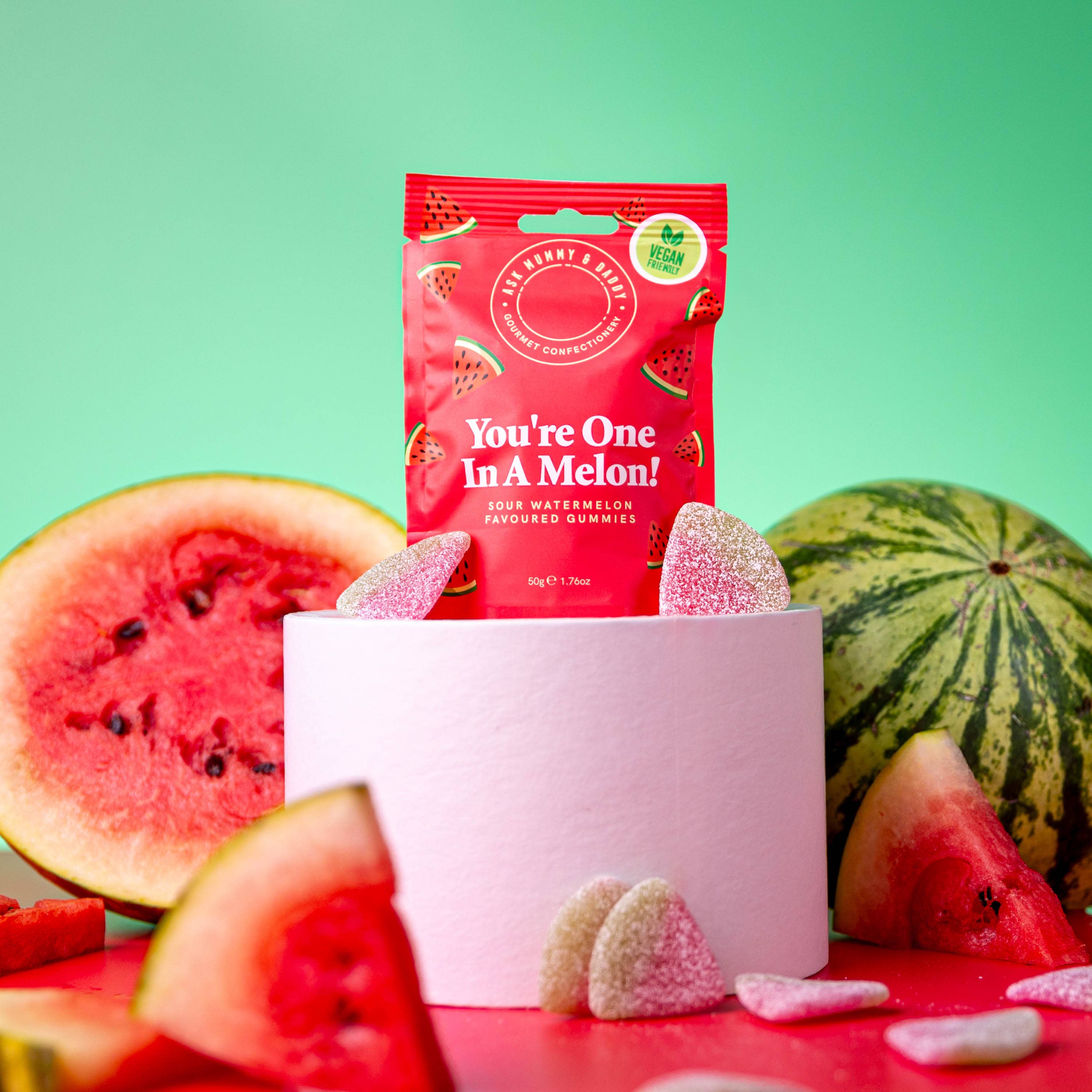 NaniManu Gummis «You’re One In A Melon!» – Beutel auf weissem Podest, davor gezuckerte Melonenschnitze