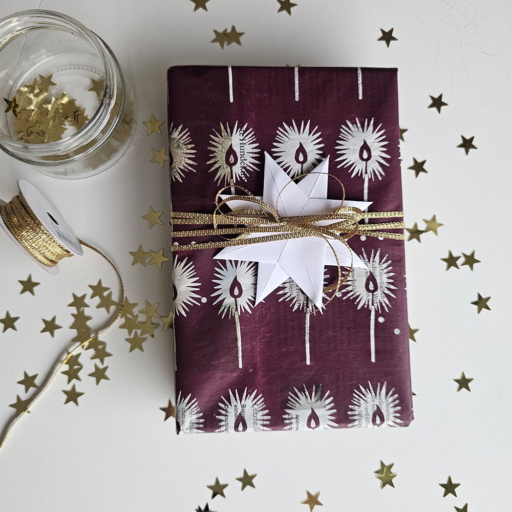 Present wrapped in «The Little Match Girl» paper with a gold ribbon and a white paper star, surrounded by small gold stars