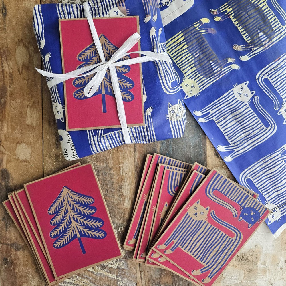 «Cat» and «Fir Tree» cards on wood, next to «Puss in Boots» wrapping paper and a wrapped present
