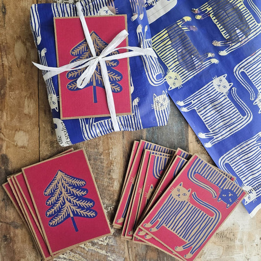 Karten «Katze» und «Tannenbaum» auf Holz, daneben Geschenkpapier «Der gestiefelte Kater» und ein verpacktes Geschenk