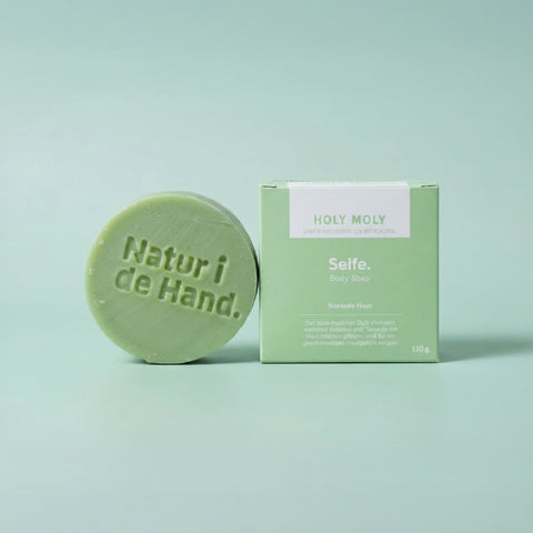 Savon naturel Holy Moly de Natur i de Hand – savon rond vert avec le logo Natur i de Hand en relief, à côté de sa boîte vert clair