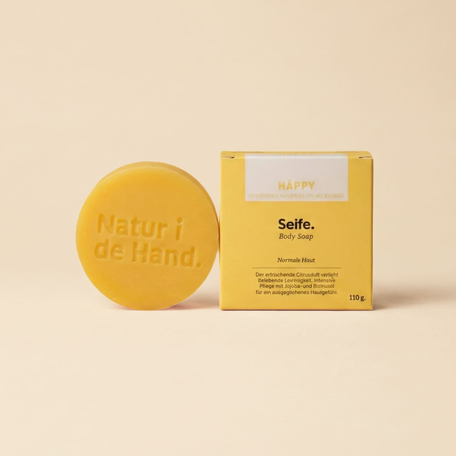 Savon naturel Häppy de Natur i de Hand – savon rond jaune avec le logo Natur i de Hand en relief, à côté de sa boîte jaune