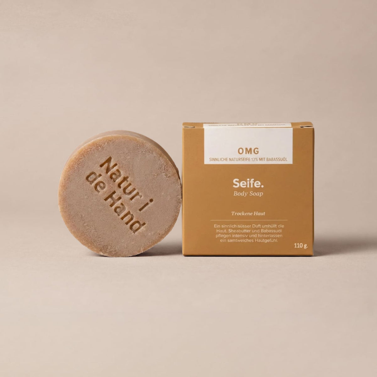 Naturseife OMG von Natur i de Hand – runde sandfarbene Seife mit Prägung «Natur i de Hand» neben ockerfarbener Schachtel