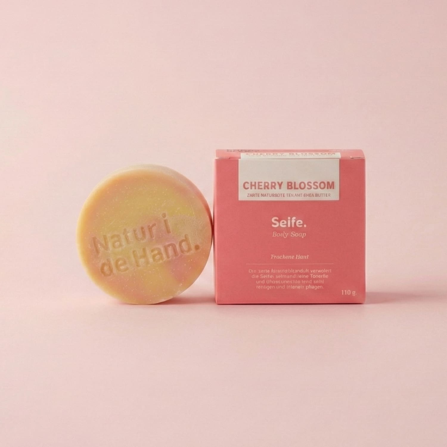 Naturseife Cherry Blossom von Natur i de Hand – runde gelb-rosa marmorierte Seife mit Prägung «Natur i de Hand» neben rosaroter Schachtel