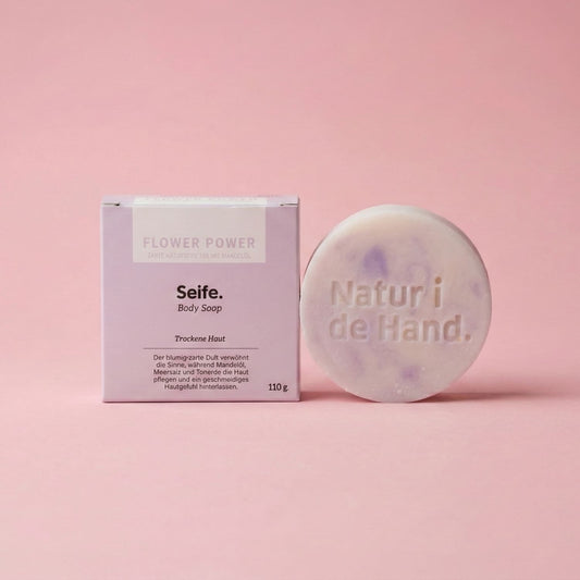 Naturseife Flower Power von Natur i de Hand – runde weiss-lila marmorierte Seife mit Prägung «Natur i de Hand» neben lila Schachtel