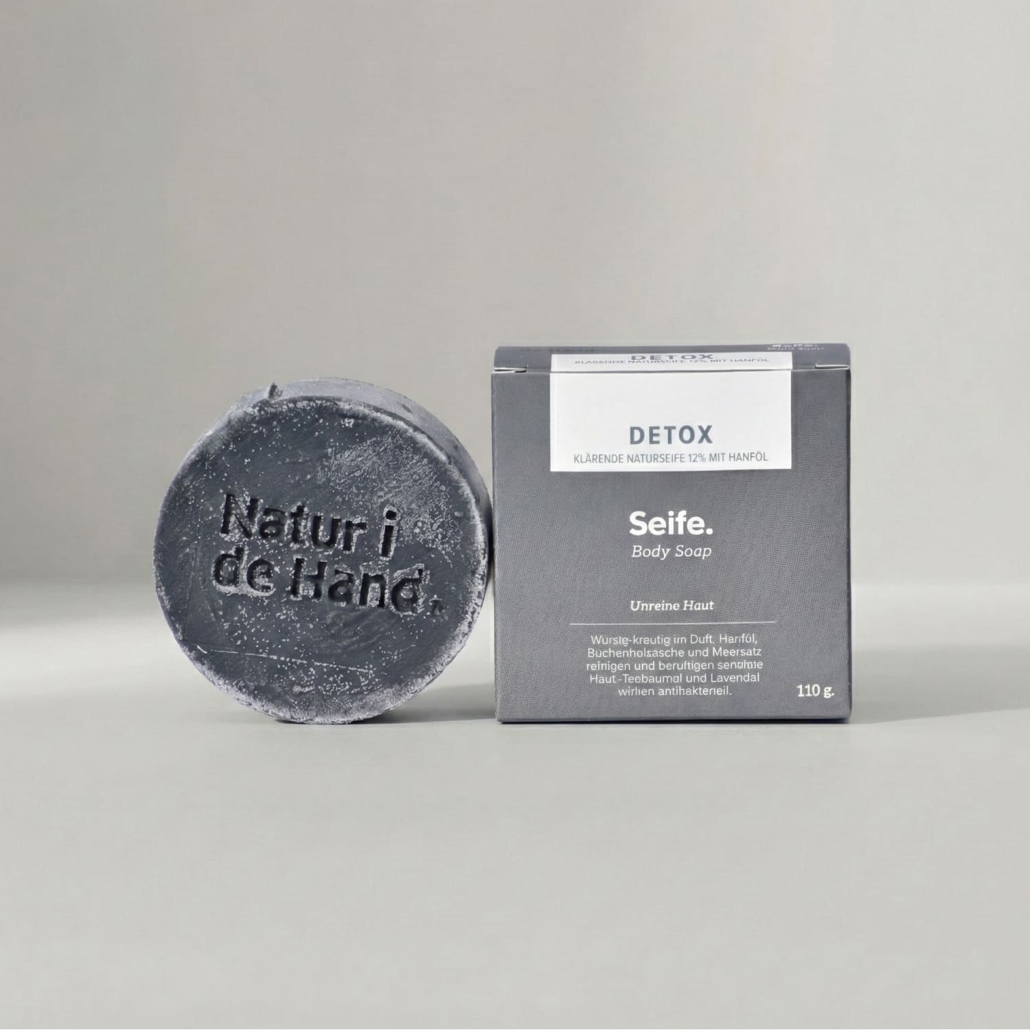 Detox natural soap by Natur i de Hand – round charcoal soap with embossed Natur i de Hand logo next to its grey box