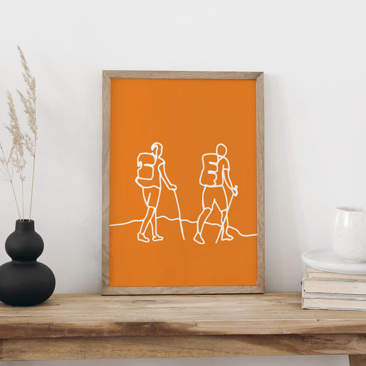 Plakat «Wandern» im hellen Holzrahmen auf einem Holztisch an weisser Wand, daneben eine schwarze Vase mit Trockengräsern und ein Bücherstapel mit Tasse