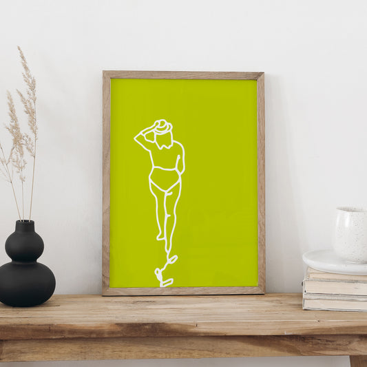 Plakat «Strandspaziergang» im hellen Holzrahmen auf einem Holztisch an weisser Wand, daneben eine schwarze Vase mit Trockengräsern und ein Bücherstapel mit Tasse
