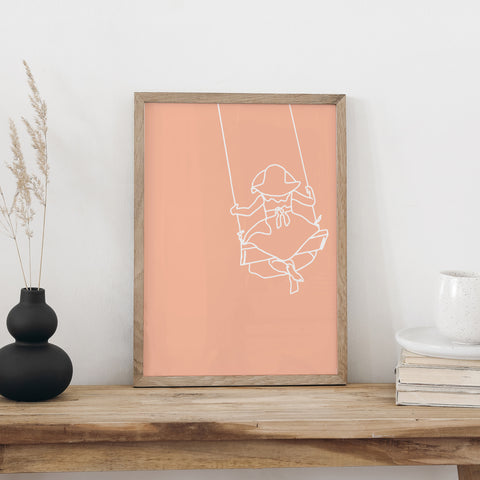 Plakat «Schaukeln» im Holzrahmen auf einer Holzbank an weisser Wand, daneben eine schwarze Vase mit Trockengräsern und ein Bücherstapel mit Tasse