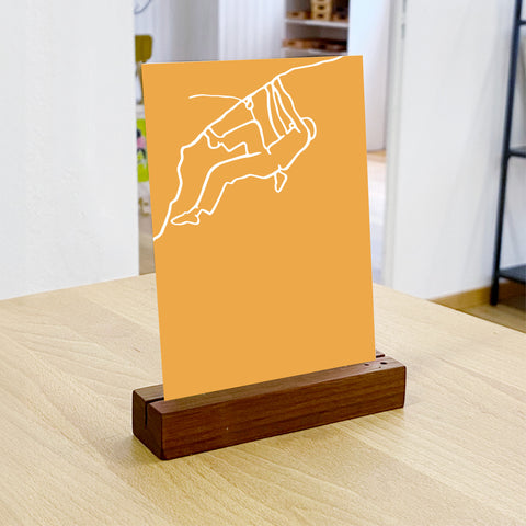NaniManu Postkarte «Klettern» im Holz-Kartenständer auf Tisch – Strichkunst-Kletterer in Szene