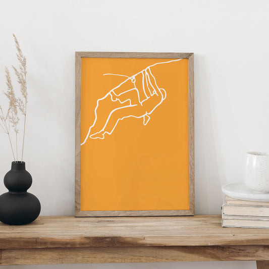 NaniManu Plakat «Klettern» im Holzrahmen auf einer Holzbank an weisser Wand, daneben schwarze Vase mit Trockengräsern und ein Bücherstapel mit Tasse