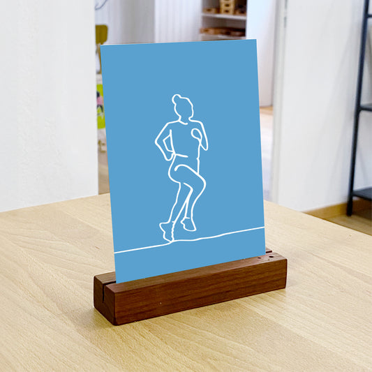 NaniManu Postkarte «Rennen» im Holzständer auf einem Tisch – StrichKunst-Läuferin, Milieu-Ansicht