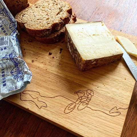 Eichen-Schneidebrett mit Brot, Bergkäse und Butter angerichtet, die Biken-Gravur im Vordergrund