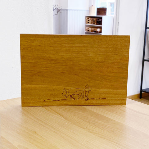 Schneidebrett Eiche Grösse S mit Strichzeichnung, aufrecht stehend auf einem Tisch in einem Raum mit Regal im Hintergrund