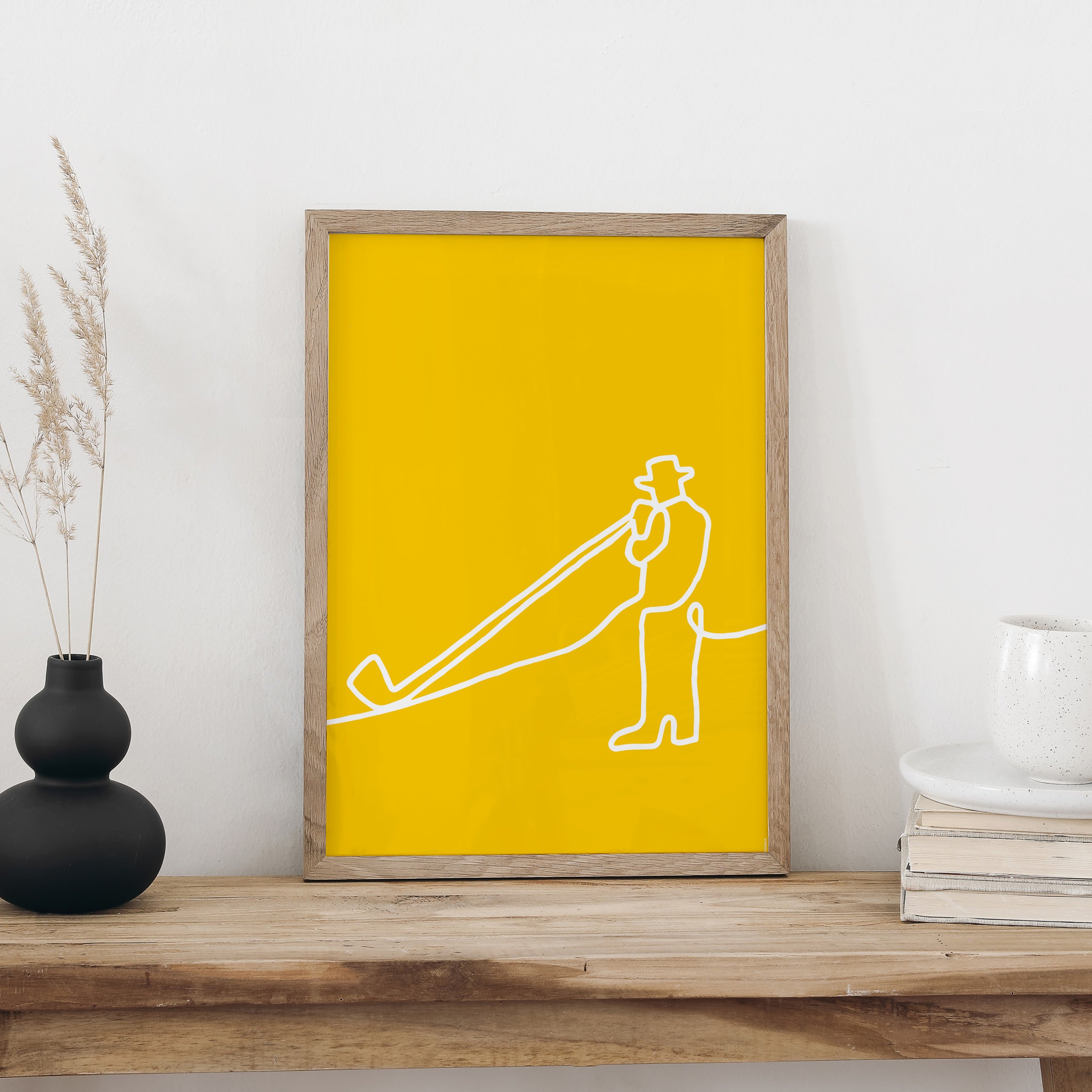 Alphorn-Plakat im Holzrahmen auf einer Holzbank vor weisser Wand, daneben eine schwarze Vase mit Trockengräsern