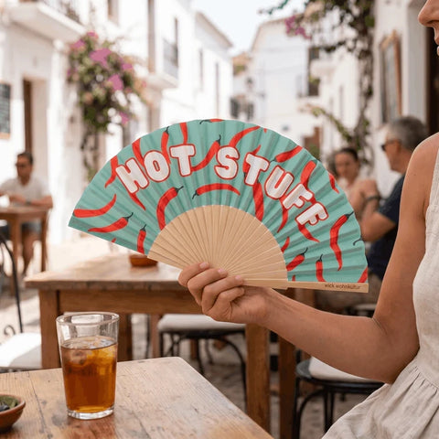 In einer weiss getünchten Gasse hält eine Frau den Fächer «Hot Stuff», davor ein Glas Eistee