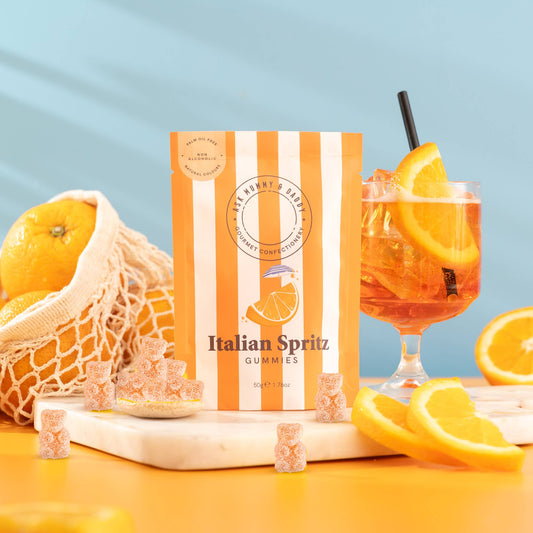 NaniManu Italian Spritz Gummis (Ask Mummy & Daddy) – orange-weiss gestreifter Beutel neben einem Spritz-Glas mit Orangenscheibe