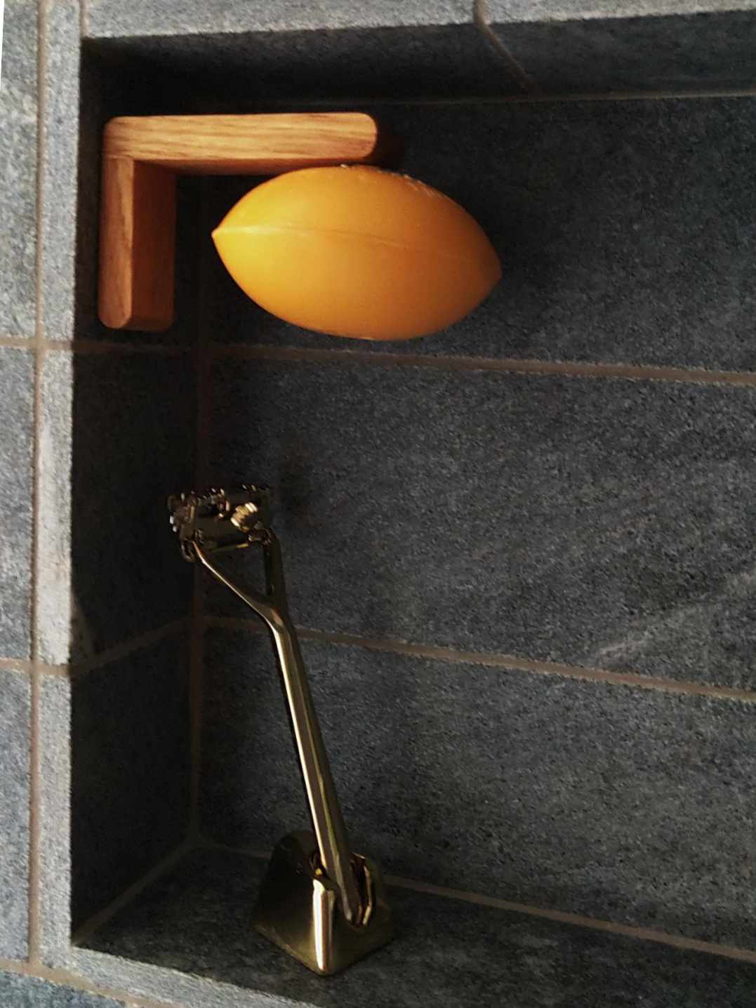Seifenhalter aus Eiche in einer Duschnische aus grauem Stein, orange Seife hängt darunter, daneben ein Rasierhobel. Motscho.ch