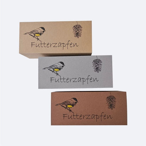 Futterzapfenbox von inclusioplus – drei Schubschachteln in Natur, Grau und Braun mit gezeichneter Meise, Zapfen und Schriftzug «Futterzapfen»